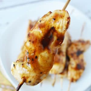 Chicken teriyaki on skewer above white plate