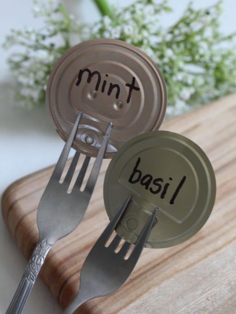 Two forks with tin can lids that say mint and basil on cutting board